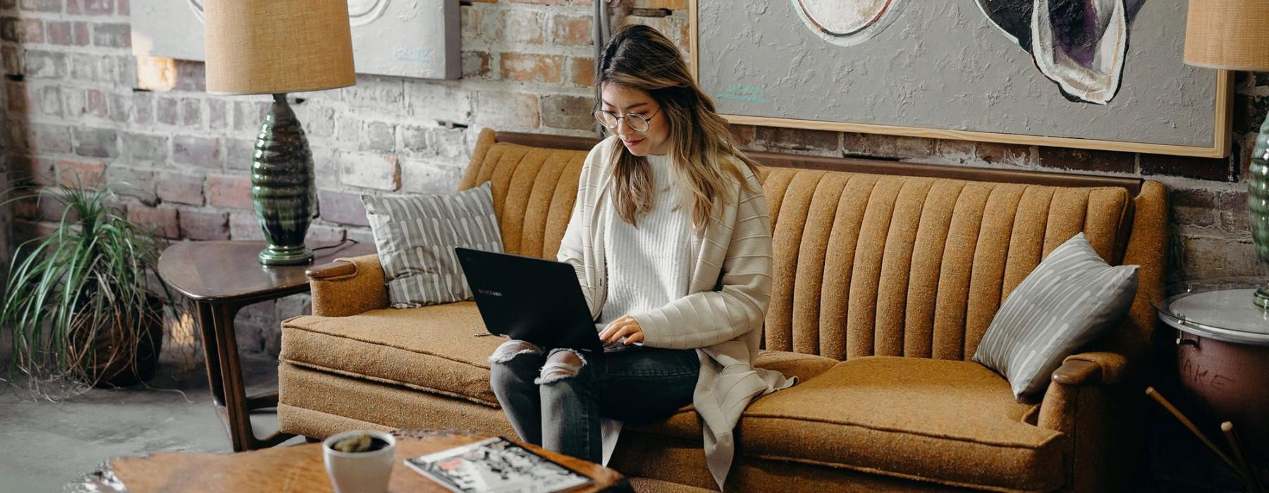 a woman sitting on a couch working on a laptop